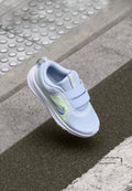 Helles blauer Sneaker mit Mesh-Obermaterial, Klettverschlussriemen, weißer Sohle und einem reflektierenden Akzent in Neon-Grün und Lila.