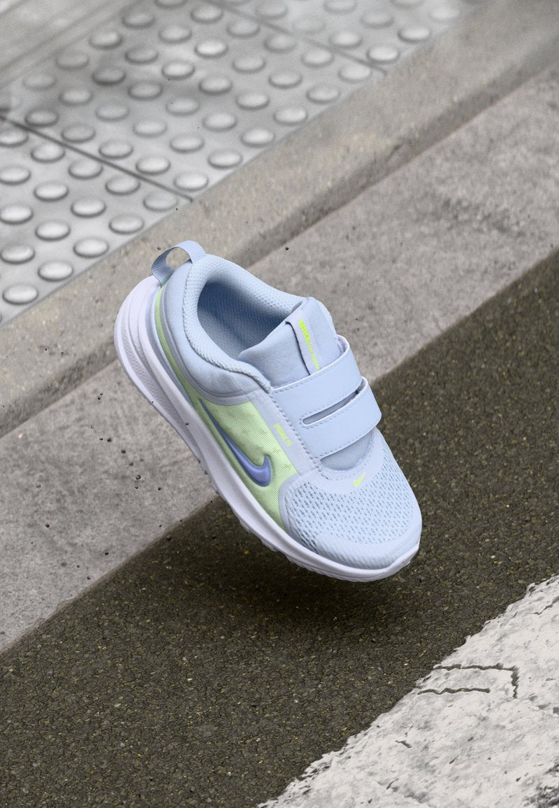 Helles blauer Sneaker mit Mesh-Obermaterial, Klettverschlussriemen, weißer Sohle und einem reflektierenden Akzent in Neon-Grün und Lila.
