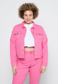Lächelnde Frau mit lockigem Haar, die eine leuchtend pinke Jacke und Hose sowie ein weißes, kurzes Shirt trägt und vor einem einfarbigen Hintergrund steht.