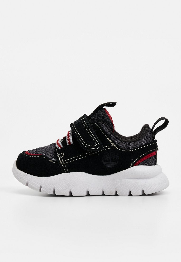 Schwarzer Sneaker mit roten Akzenten, einer strukturierten Oberseite und Klettverschluss, weißer Sohle und einem runden Logo an der Seite.
