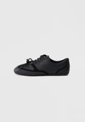 Schwarzer Sneaker mit niedrigem Profil, Schnürung, glatter und glänzender Oberfläche, minimalen Nähten und flacher Sohle auf schlichtem Hintergrund.