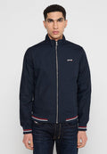 Navyblaue Jacke mit Stehkragen, Frontreißverschluss, rot-weißen Streifenakzenten an den Bündchen und dem Saum, aus einem glatten, leichten Material gefertigt.