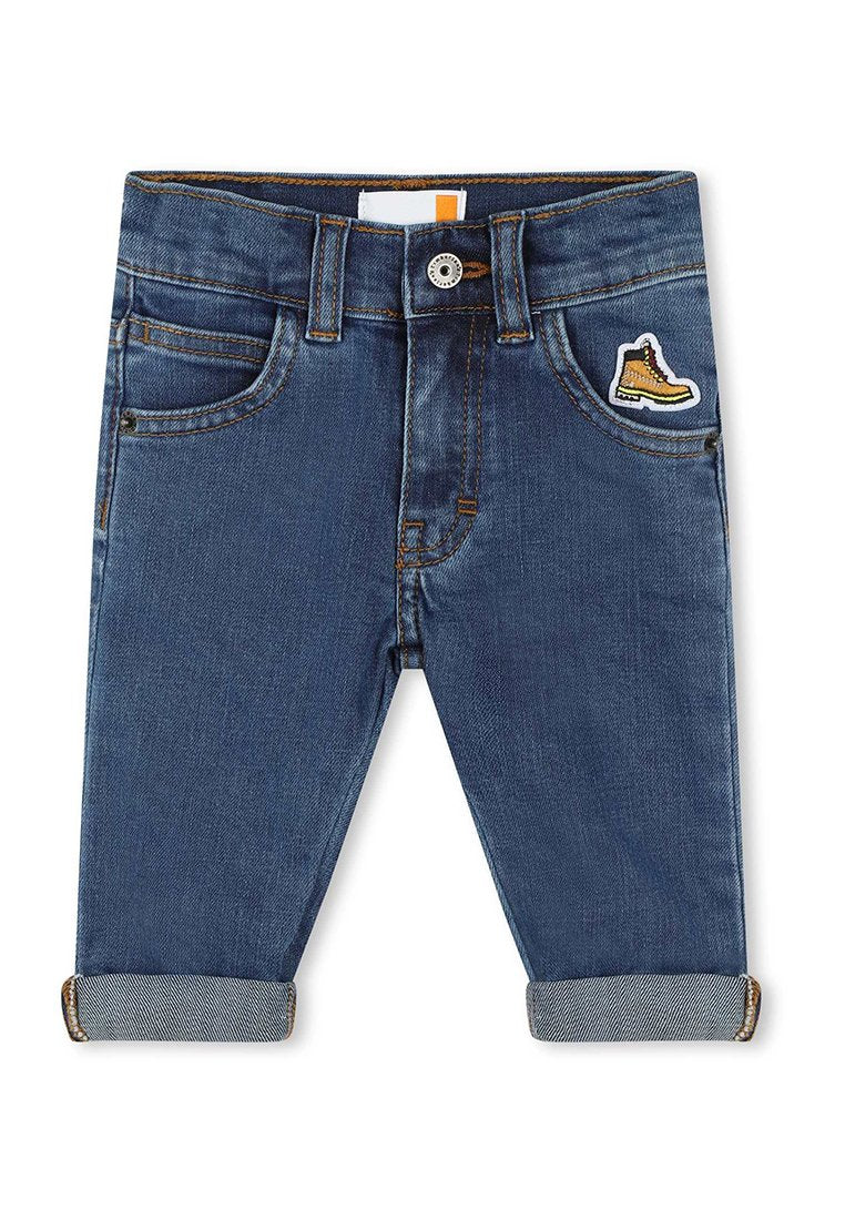 Dunkelblaue Jeans mit eng anliegendem Schnitt, mit umgeschlagenen Säumen und einem Logo-Patch eines Stiefels auf der rechten Tasche.