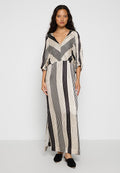Maxikleid in Creme mit schwarzen vertikalen Streifen. V-Ausschnitt, weite Ärmel und seitliche Schlitze. Weicher Stoff, leicht lockere Passform. Schwarze Schuhe getragen.