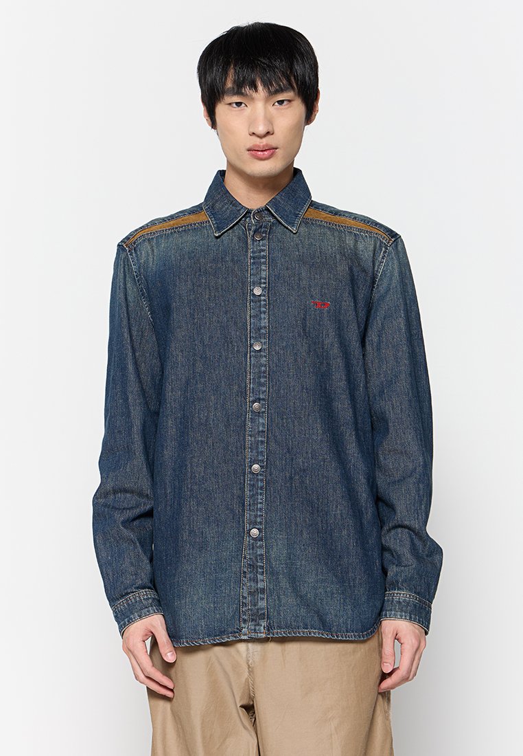 Dunkelblaue Jeanshemd mit Knopfleiste, spitzem Kragen und kontrastierender brauner Naht an den Schultern. Verfügt über ein kleines rotes Logo.