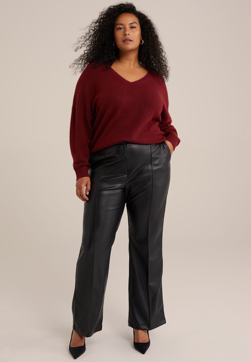 Bordeauxfarbener Pullover mit V-Ausschnitt, kombiniert mit schwarzen Lederhosen mit geradem Schnitt und sichtbaren Nähten. Schwarze High Heels vervollständigen den Look.