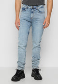 Mann trägt hellblaue Slim-Fit-Jeans und schwarze Schnürschuhe und steht vor einem schlichten weißen Hintergrund.