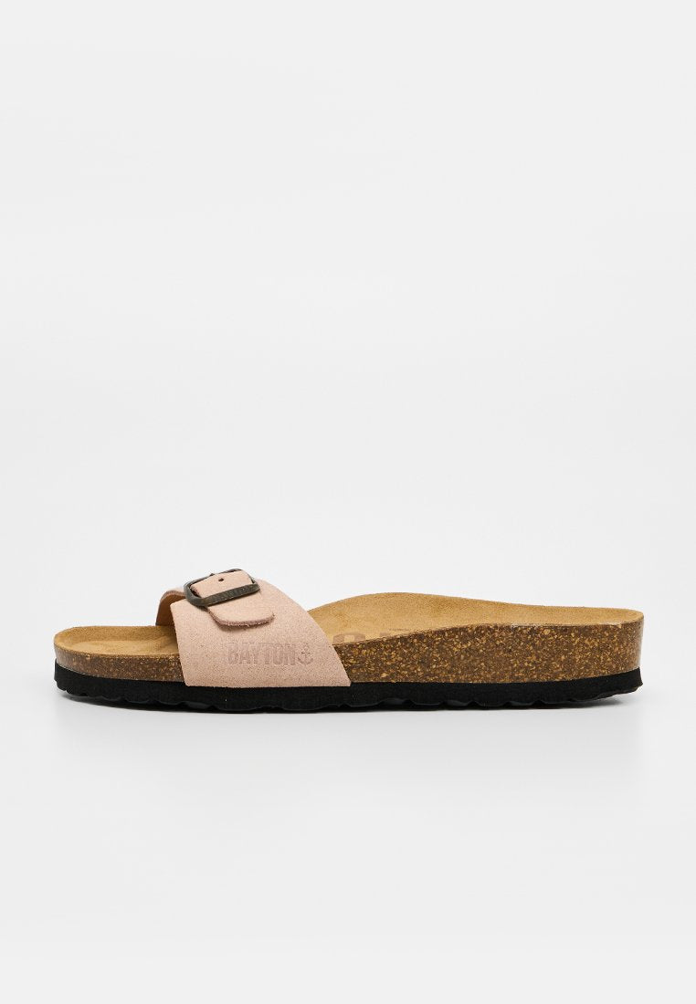 Beige Wildleder-Slidesandale mit einem verstellbaren Riemen, Kork-Fußbett und schwarzer strukturierter Sohle, von der Seite auf weißem Hintergrund gezeigt.