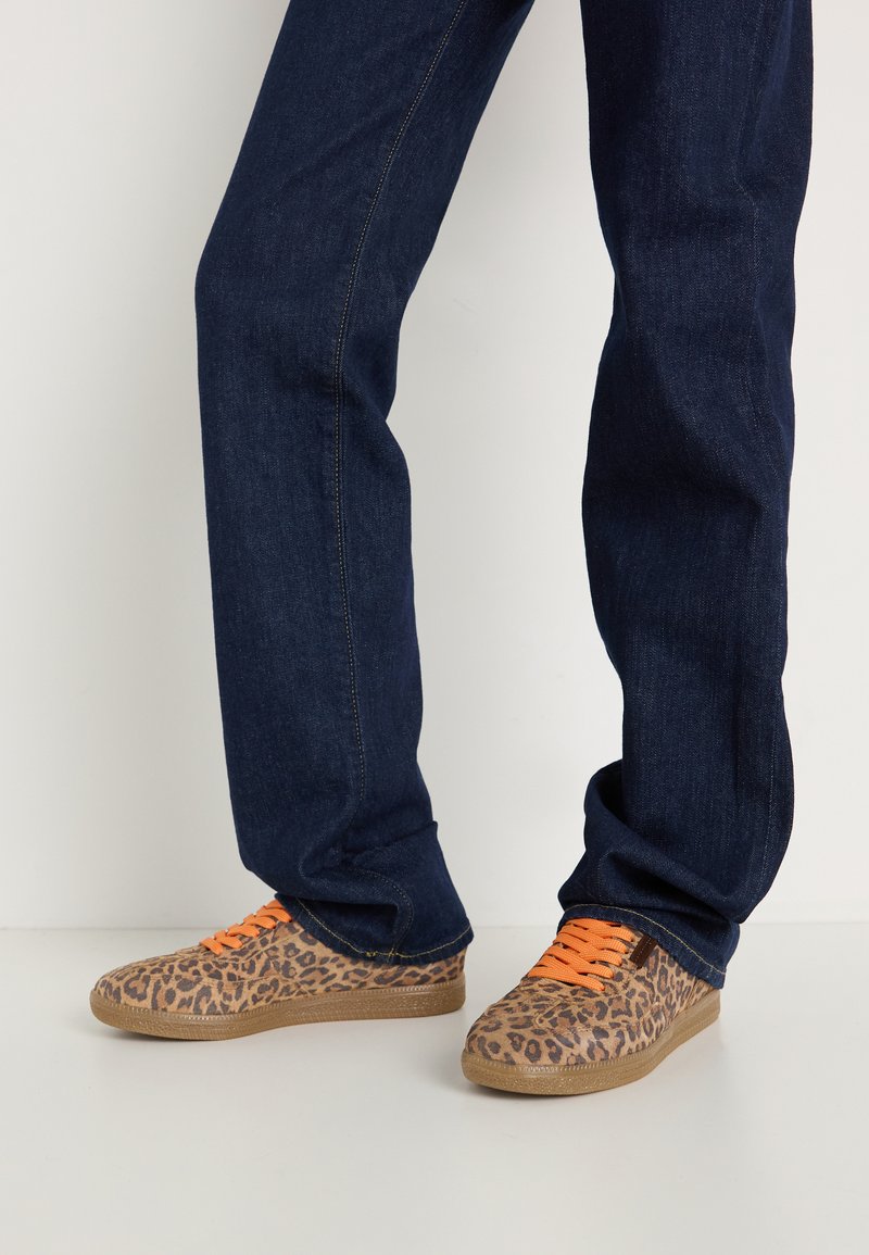 Sneaker mit Leopardenmuster und orangefarbenen Schnürsenkeln, Obermaterial aus strukturiertem Stoff und einer hellbraunen Gummisohle, kombiniert mit dunkelblauen Jeans.