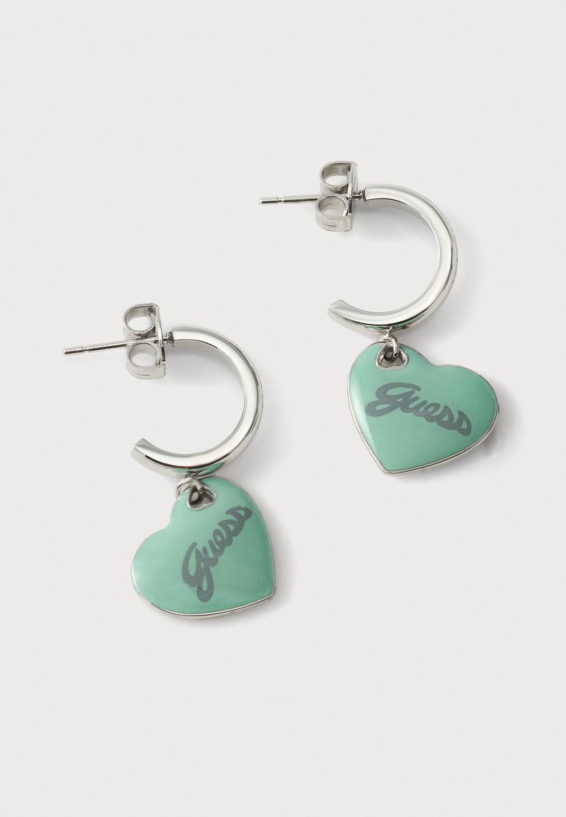 Silberne Creolen mit mintgrünen herzförmigen Anhängern, graviert mit dem Wort "Guess" in Schriftzug.