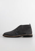 Graue Wildleder-Chukka-Stiefel mit abgerundeter Zehe, zwei Ösen zum Schnüren, kontrastierenden hellen Nähten entlang der Sohle und einer strukturierten Oberfläche.