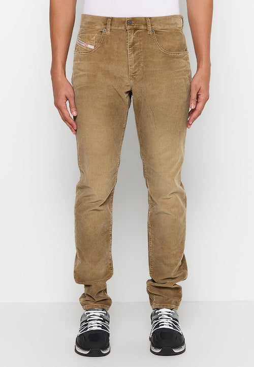Beige Cord-Hosen mit schmalem Schnitt, Fronttaschen und einem kleinen Logostick. Weiches Material mit subtiler Rippstruktur, kombiniert mit schwarzen Sportschuhen.