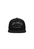 Schwarze Kappe mit gesticktem Text "LES DEUX" und "Est. 2011" in Weiß, mit dekorativen Elementen. Starre Krempe und verstellbarer Riemen auf der Rückseite.
