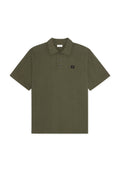 Olivgrünes Poloshirt mit kurzen Ärmeln, drei Knöpfen und kleinem schwarzem quadratischem Patch mit der römischen Zahl II auf der Brust.
