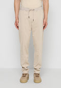 Beige Freizeithose mit elastischem Tunnelzug am Bund, kombiniert mit braunen Wildledersneakern, von der Taille bis zu den Füßen auf neutralem Hintergrund abgebildet.