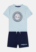 Himmelblaues kurzärmliges Hemd mit einem runden Logo, kombiniert mit marineblauen Shorts mit Kordelzug und Logodetail. Aus weichem Baumwollmix.