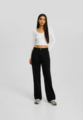 Schwarze weit geschnittene Jeans aus Denim, kombiniert mit einem engen weißen Langarmoberteil. Das Outfit wird mit grauen Sneakers abgerundet.