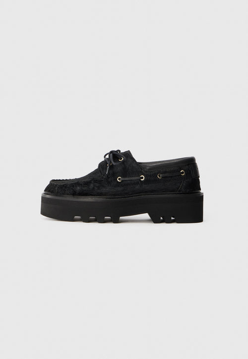 Schwarze Schuhe mit einer klobigen Plateausohle und einem strukturierten Pelzfinish. Verfügt über runde Schnürsenkel, goldene Ösen und eine strukturierte Gummisohle.