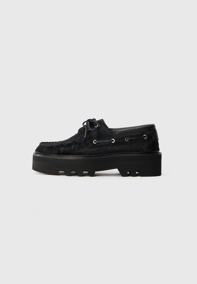 Schwarze Schuhe mit einer klobigen Plateausohle und einem strukturierten Pelzfinish. Verfügt über runde Schnürsenkel, goldene Ösen und eine strukturierte Gummisohle.