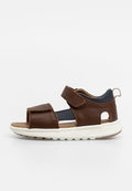 Braune Leder-Sandalen mit strukturiertem Finish, verstellbaren Riemen, einer weißen Sohle und einem Ausschnitt an der Außenseite.