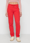 Person in roten Kordelzug-Sweatpants, beigen Sneakers und einem cropped langärmligen rosa Oberteil, stehend vor einem weißen Hintergrund.