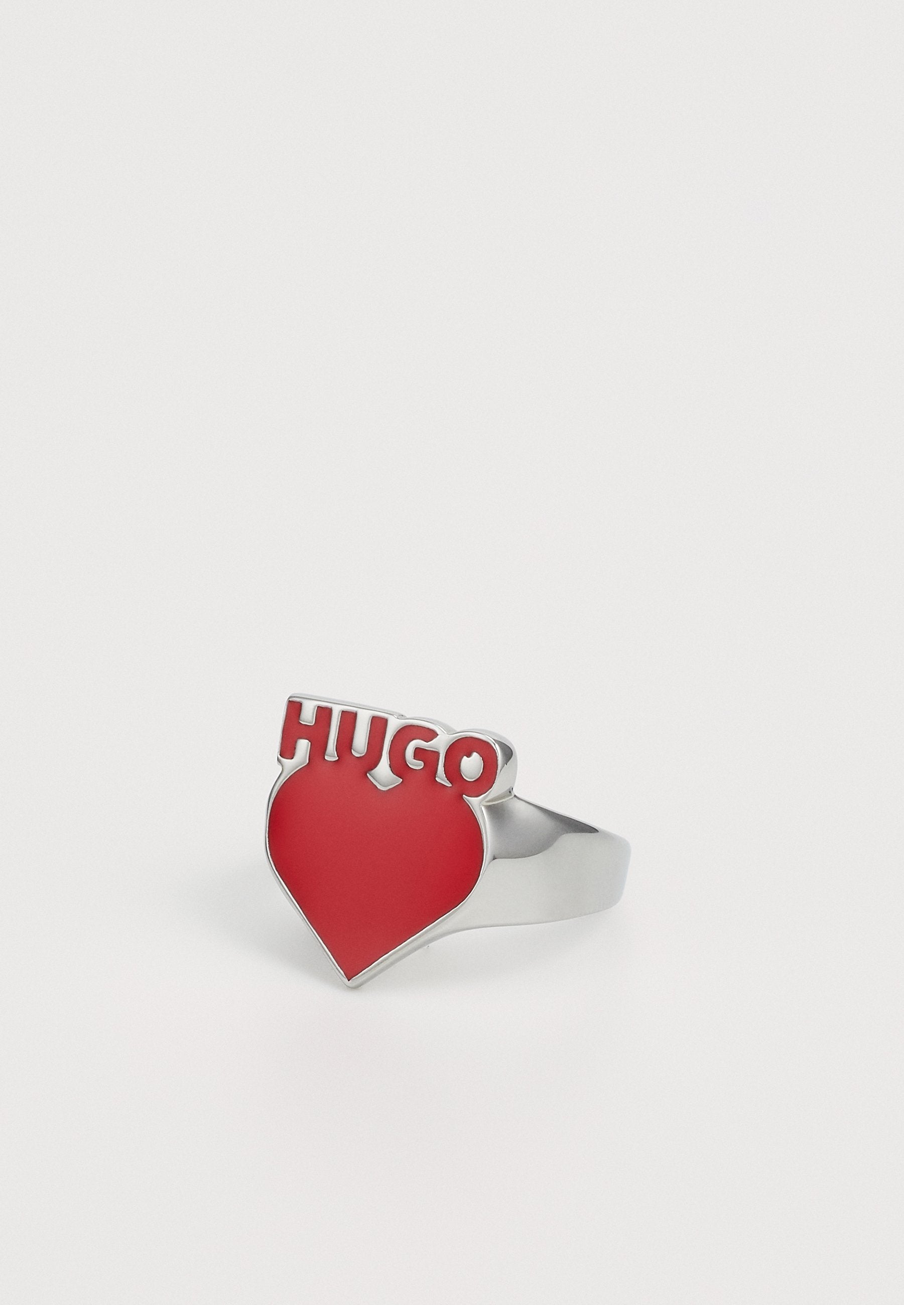 Silberring mit einer auffälligen roten Herzform und dem Wort "HUGO" in fetten, erhabenen Buchstaben oben. Glatte Oberfläche mit glänzenden Akzenten.