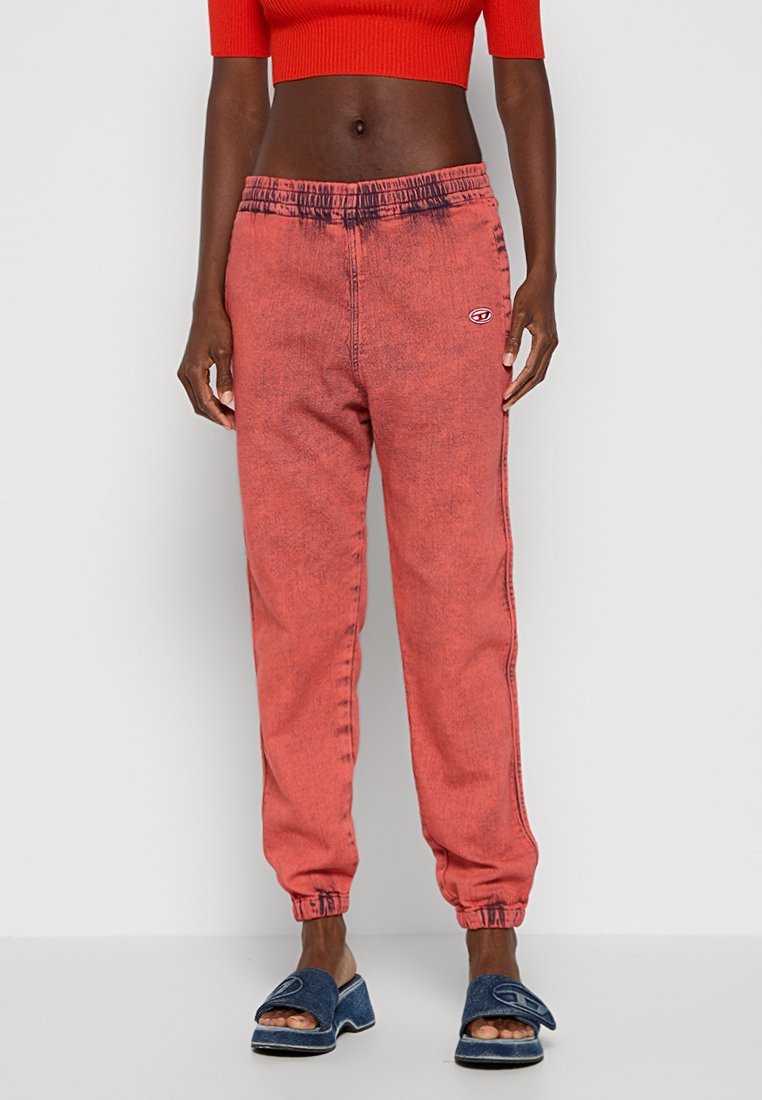 Rote Denim-Jogginghosen mit elastischem Bund, gepolsterten Knöcheln und einem kleinen Logo am linken Oberschenkel, das eine verblasste Textur aufweist.