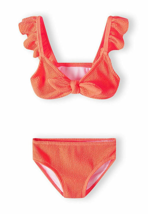 Zweiteiliges Bikini-Set in leuchtendem Korallenrot. Das Oberteil hat Rüschenträger und eine Schleifendetail auf der Vorderseite, während der Unterteil einen klassischen Schnitt mit strukturiertem Stoff aufweist.