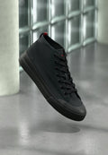 Schwarzer Sneaker in hoher Schnittform mit Obermaterial aus Canvas, rundem Zehenbereich und tonalen Schnürsenkeln. Verfügt über eine Gummisohle und ein kleines rotes Akzent am Absatz.