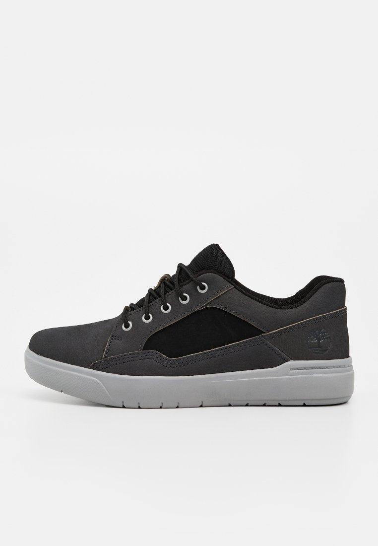 Dunkler Sneaker in Grau und Schwarz mit schwarzen Schnürsenkeln und hellgrauer Sohle, Seitenansicht zeigt Timberland-Logo an der Ferse.