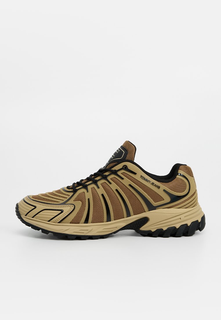Beiger Laufschuh mit einem Obermaterial aus Mesh, schwarzen Akzenten, einer strukturierten Sohle und einem stromlinienförmigen Design mit geschwungenen Linien und verstärkten Bereichen.