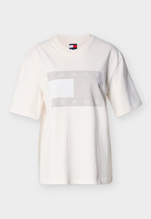 Hellcremefarbenes Baumwoll-T-Shirt mit kurzen Ärmeln, das ein graues rechteckiges Motiv mit dem Text "TOMMY JEANS" zeigt. Rundhalsausschnitt.
