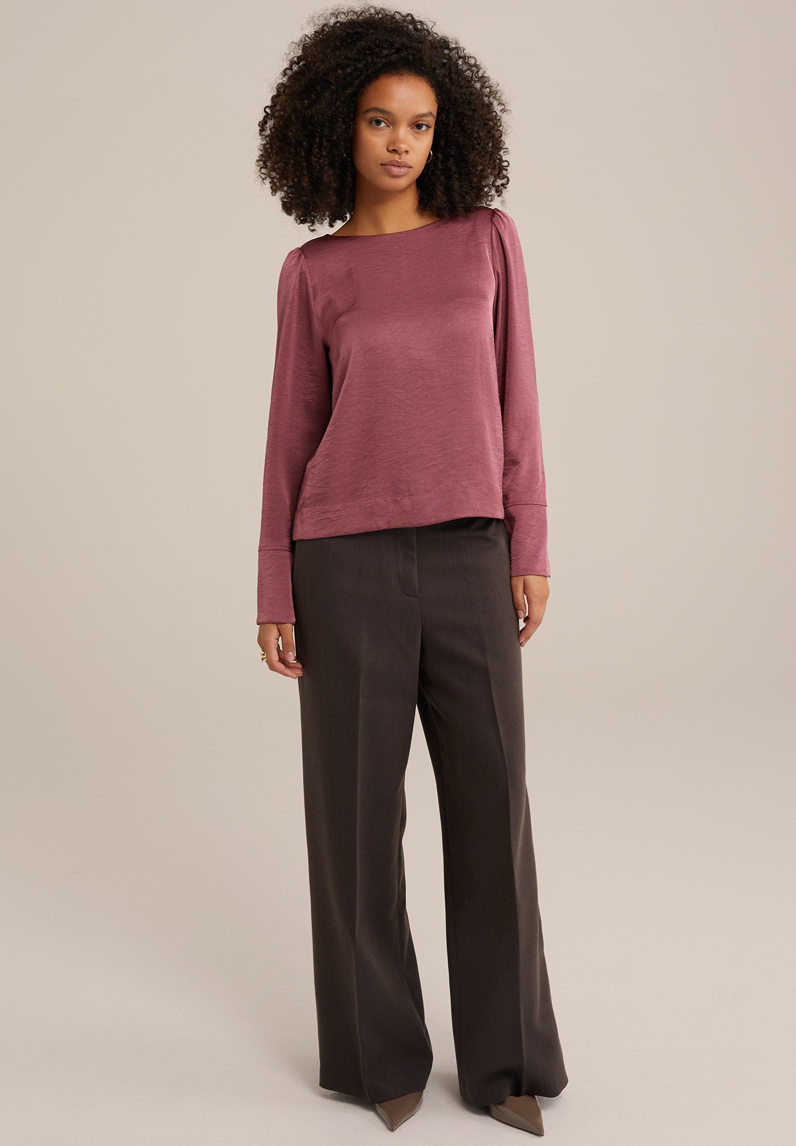 Langärmlige Bluse in Mauve mit lockerem Schnitt und strukturierter Oberfläche, kombiniert mit hoch geschnittenen, maßgeschneiderten dunklen Hosen und spitzen Schuhen.