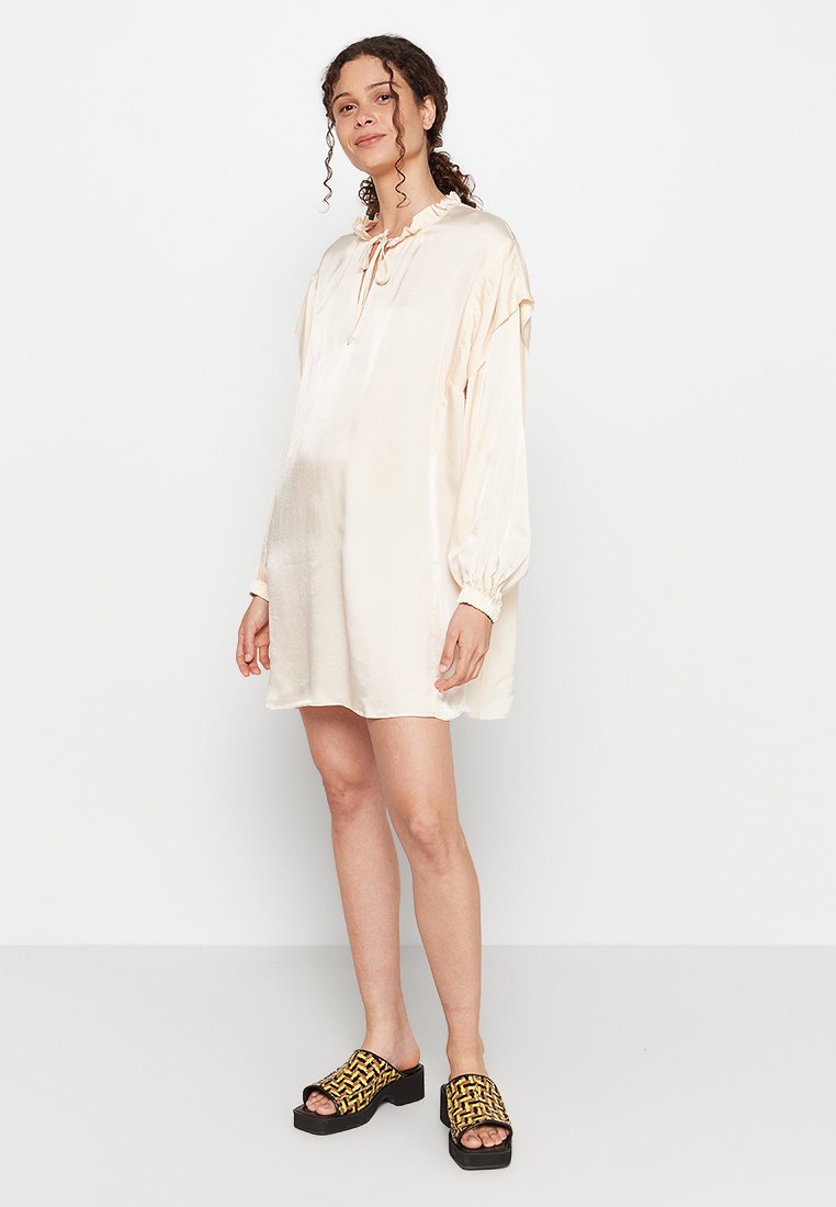 Seidencreme-Kleid mit Kordelzug-Ausschnitt, langen Puffärmeln und lockerer Passform, kombiniert mit schwarz-gelben Plateausandalen.
