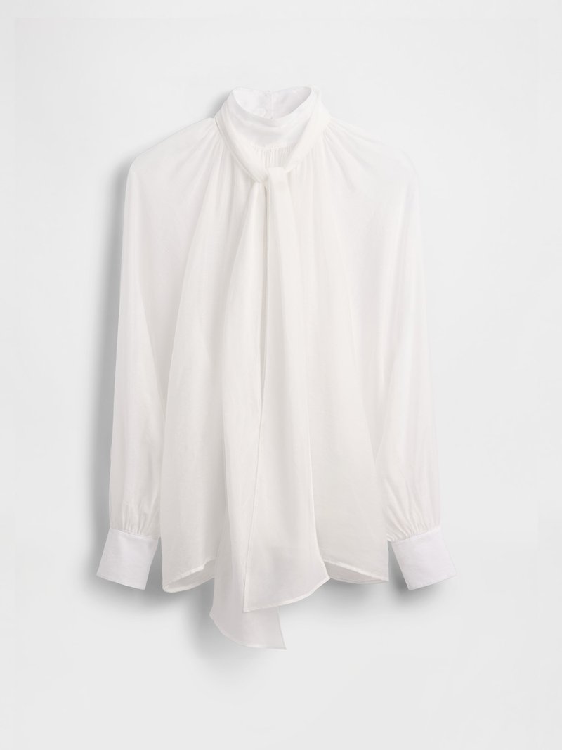 Weiße Bluse mit hohem Kragen, vorne fließend, lange Ärmel und geknöpfte Manschetten. Hergestellt aus einem leichten, transparenten Stoff.