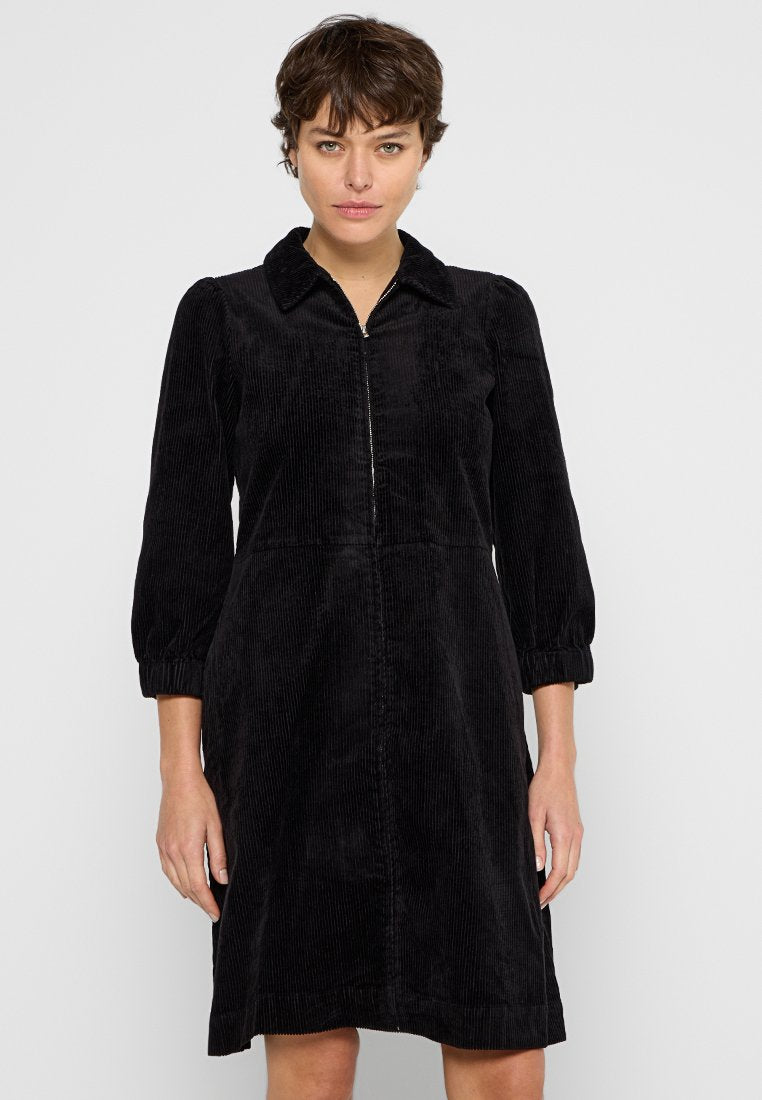 Schwarzes Cordkleid mit kragenförmigem Ausschnitt, Reißverschluss vorne, Dreiviertelärmeln und ausgestellt Rock. Weiche Textur mit vertikalen Rillen.