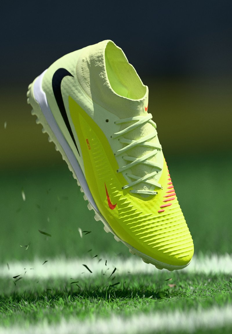 Helles gelbes Sportschuh mit strukturiertem Obermaterial, weißer Sohle, schwarzen und roten Akzenten. Für Kunstrasen konzipiert, mit Schnürsenkeln und einer flachen Silhouette.