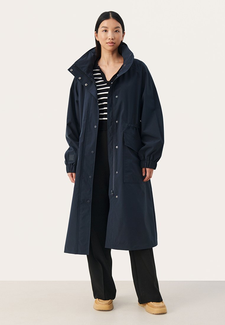 Marineblauer wasserdichter langer Mantel mit hohem Kragen, elastischen Bündchen und Druckknopfverschlüssen vorne. Verfügt über Taschen an den Seiten und einen entspannten Schnitt.