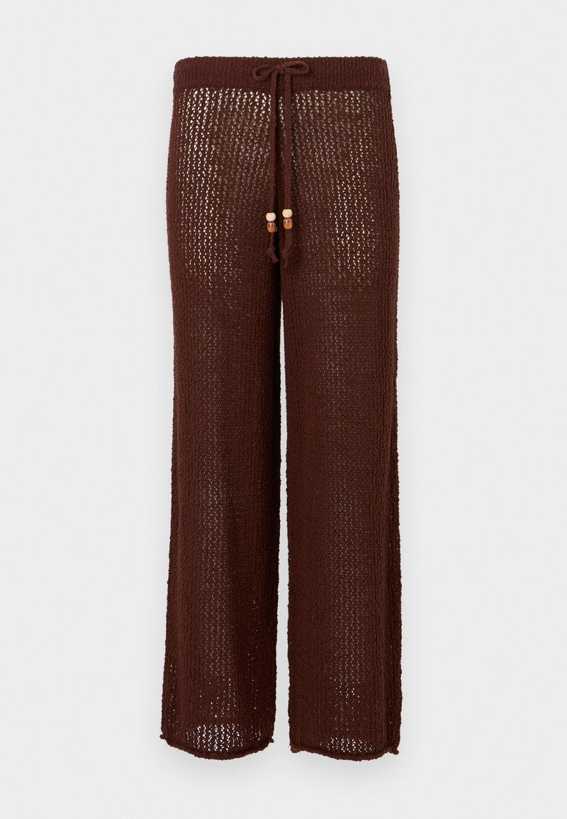 Braune, gestrickte, weit geschnittene Hose mit einem Kordelzugbund und Holzkugeln als Akzent. Der Stoff ist semi-transparent und hat ein strukturiertes Muster.