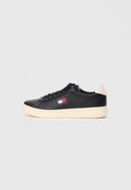 Schwarze Ledersneaker mit abgerundetem Zehenbereich, cremefarbener Sohle und einem kleinen Logo-Patch in Rot, Weiß und Blau an der Seite. Weicher beiger Fersenlasche.