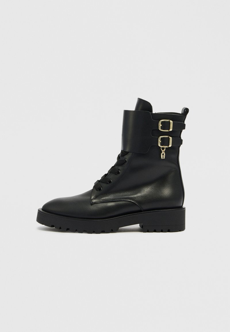 Schwarzer Leder-Stiefelette mit abgerundetem Zehenbereich, Schnürung vorne und zwei goldenen Schnallenakzenten an einer breiten Manschette. Verfügt über eine profilierte, griffige Sohle.