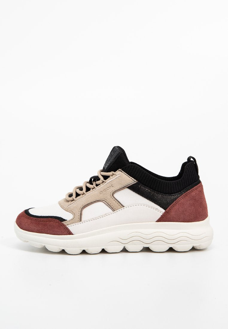 Sneaker mit einem Obermaterial aus weißem und beigem Leder, schwarzen Textilakzenten und einer burgunderroten Wildlederferse. Dicke weiße Gummisohle mit Wellenmuster.