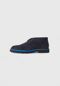 Marineblaue Wildleder-Stiefeletten mit runder Zehenpartie, kontrastierender blauer Außensohle und minimalistischem Schnürdesign; die Textur wirkt weich und edel.