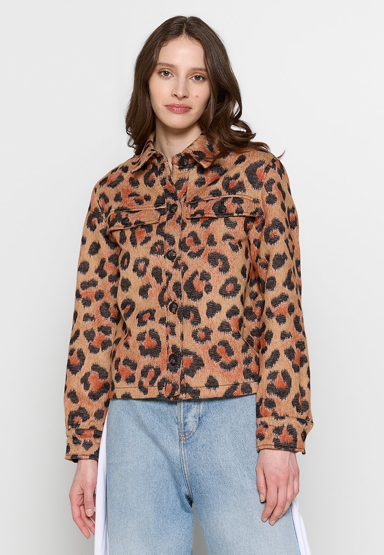 Leopardenprint-Denimjacke mit Knopfverschluss, zwei Brusttaschen, Kragen und cropped Design. Beige- und Orangetöne dominieren.