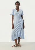 Hellblaues Wickelkleid mit strukturiertem Muster, kurzen Schmetterlingsärmeln und gerafftem Saum, kombiniert mit weißen Sandalen.
