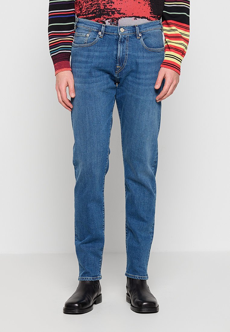 Blaue Jeans aus Denim mit schmaler Passform, ausgestattet mit einem Fünf-Taschen-Design, Metallknopfverschluss und dezent verwaschener Textur. Kombiniert mit schwarzen Stiefeletten.