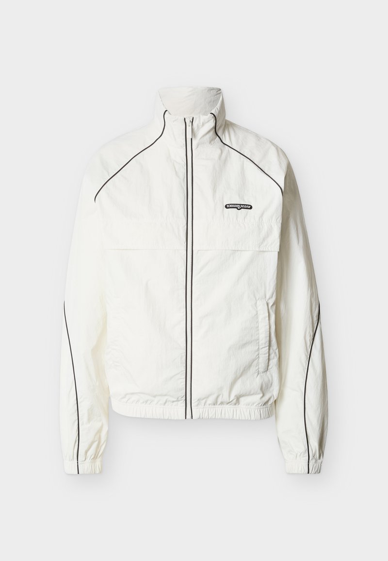 Weiße leichte Jacke mit hohem Kragen, schwarzen Paspeln entlang der Nähte und einem durchgehenden Reißverschluss vorne. Mit einem Logo auf der oberen linken Seite.