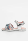 Silberne Sandalen mit glitzerndem Design, ausgestattet mit über Kreuz verlaufenden Riemen in Silber und blauen Funken, einer weichen rosa Innensohle und einer strukturierten weißen Außensohle.