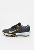 Schwarze und graue Sportschuhe mit einer strukturierten Oberseite, ausgestattet mit einem goldenen Swoosh, schwarzen Schnürsenkeln und einer weißen Zwischensohle mit gelben Akzenten.