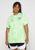 Hellgrünes Sporttrikot aus atmungsaktivem Material, mit einem auffälligen grafischen Muster und einem blauen Logo auf der Brust. Kurze Ärmel, lockerer Sitz.